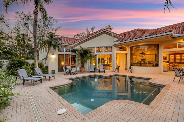 back of property with a tiled roof, stucco siding, a fenced in pool, and a patio area