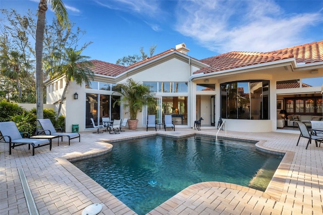 rear view of property with a tiled roof, stucco siding, an outdoor pool, and a patio