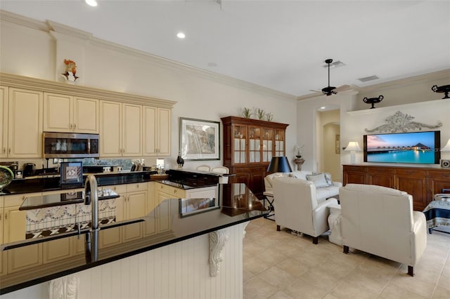 kitchen with dark countertops, arched walkways, cream cabinetry, stainless steel microwave, and open floor plan