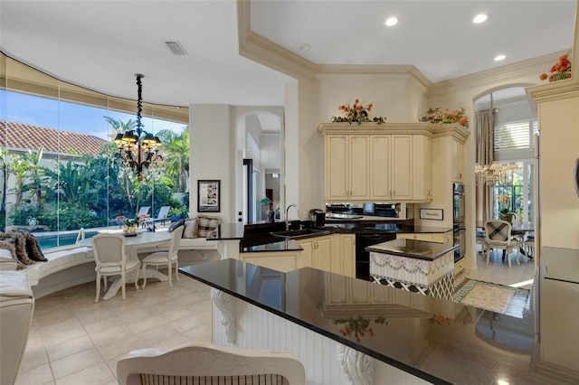 kitchen featuring visible vents, a chandelier, arched walkways, cream cabinetry, and a sink