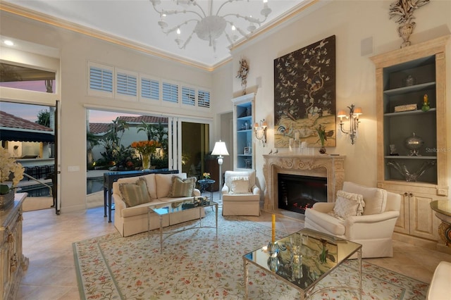 living area with built in features, a high end fireplace, ornamental molding, a towering ceiling, and a notable chandelier