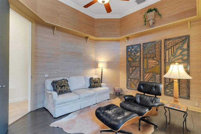 living area with wood finished floors, visible vents, a ceiling fan, baseboards, and ornamental molding