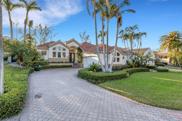 mediterranean / spanish-style house with a tiled roof, a front yard, stucco siding, decorative driveway, and an attached garage