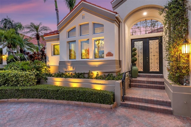 exterior entry at dusk featuring stucco siding and a tiled roof