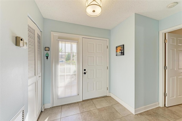 foyer with light tile patterned floors, visible vents, a textured ceiling, and baseboards