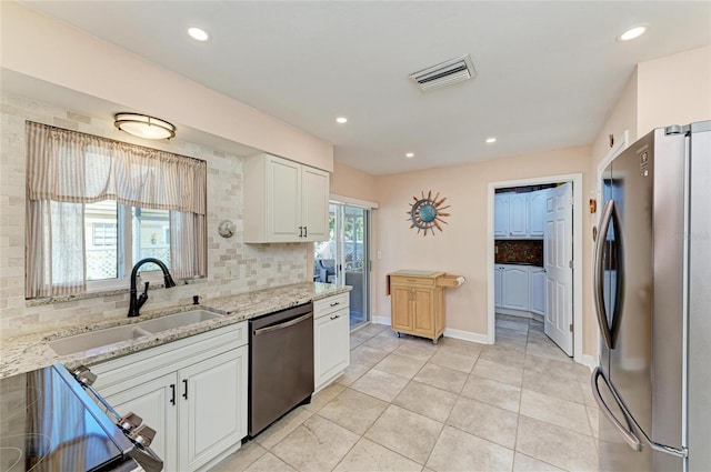 kitchen featuring visible vents, light stone countertops, white cabinets, stainless steel appliances, and a sink