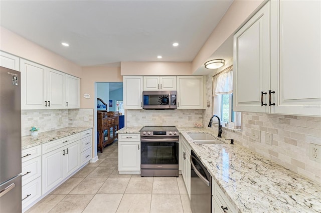 kitchen featuring light stone countertops, light tile patterned flooring, a sink, white cabinets, and appliances with stainless steel finishes