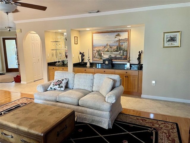 living room featuring visible vents, baseboards, ornamental molding, arched walkways, and a ceiling fan