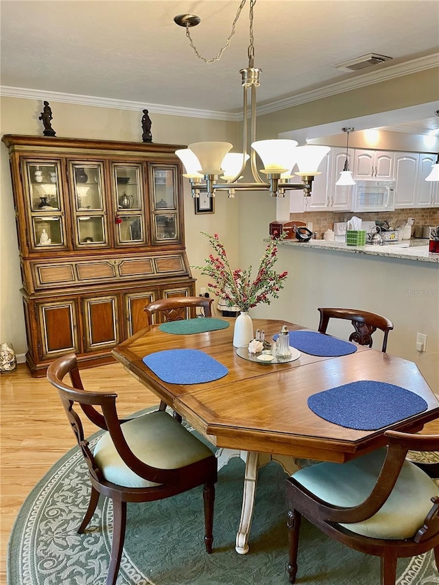 dining room with crown molding, visible vents, light wood finished floors, and a chandelier