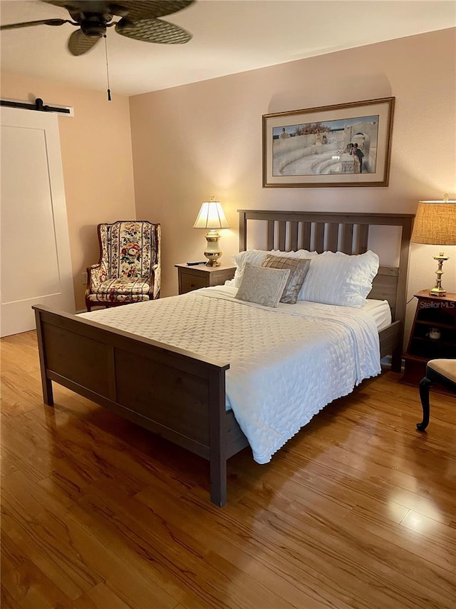 bedroom featuring ceiling fan, a barn door, and wood finished floors