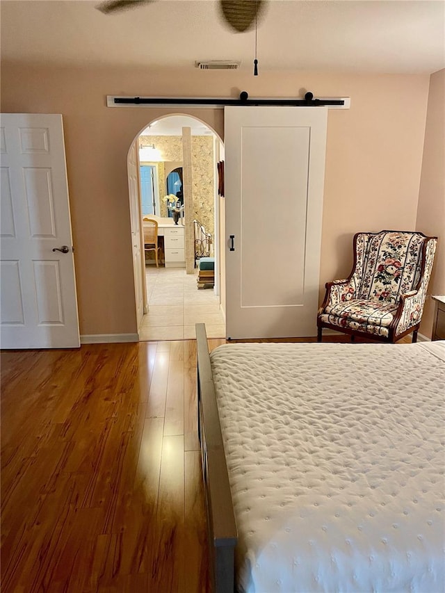 bedroom featuring wood finished floors, visible vents, baseboards, arched walkways, and a barn door