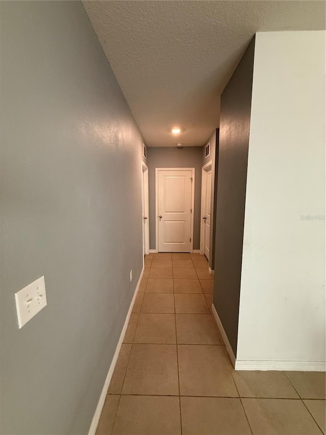 hall featuring light tile patterned flooring, a textured ceiling, and baseboards