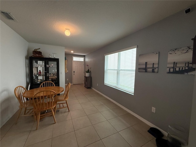 dining space featuring a textured ceiling, light tile patterned flooring, visible vents, and baseboards