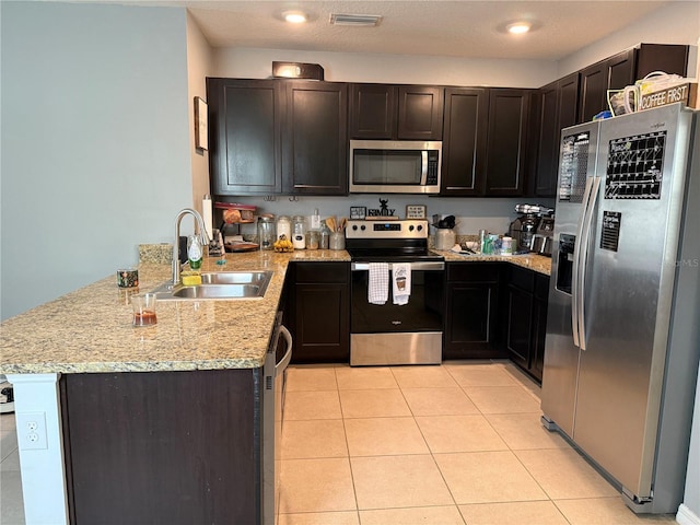 kitchen featuring light tile patterned floors, a peninsula, a sink, visible vents, and appliances with stainless steel finishes