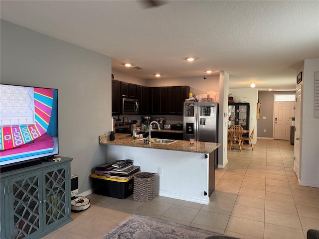 kitchen featuring light tile patterned floors, appliances with stainless steel finishes, dark stone countertops, a peninsula, and a sink