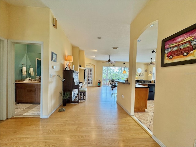 corridor featuring baseboards, light wood-type flooring, arched walkways, and visible vents