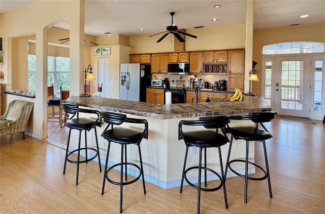 kitchen with a ceiling fan, a breakfast bar, decorative backsplash, black electric range, and stainless steel fridge