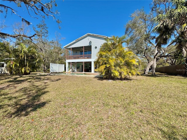 back of property featuring a yard, an outdoor pool, a balcony, and fence