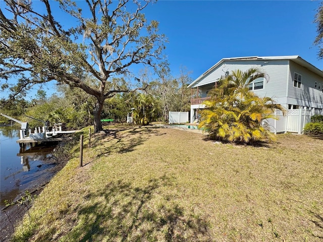 view of yard featuring an outdoor pool, a water view, a boat dock, and fence