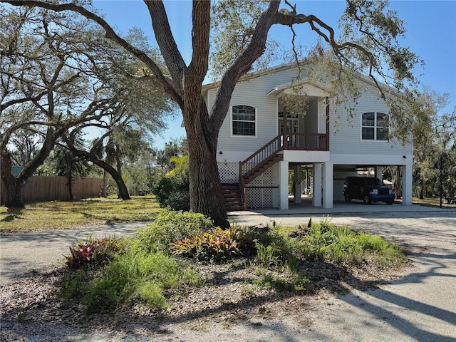 coastal home with a carport, stairway, fence, and driveway