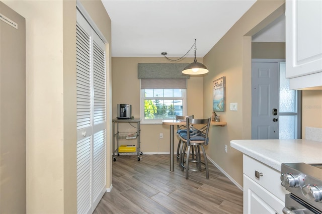 kitchen featuring baseboards, light wood-style flooring, stainless steel electric range, light countertops, and white cabinetry