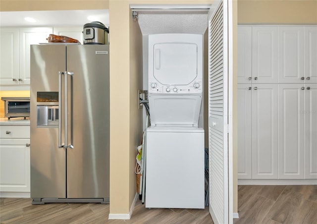 washroom featuring laundry area, a textured ceiling, stacked washing maching and dryer, and light wood-type flooring