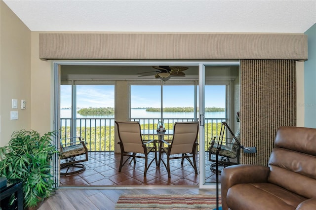 dining area with wood finished floors, a textured ceiling, ceiling fan, and a water view