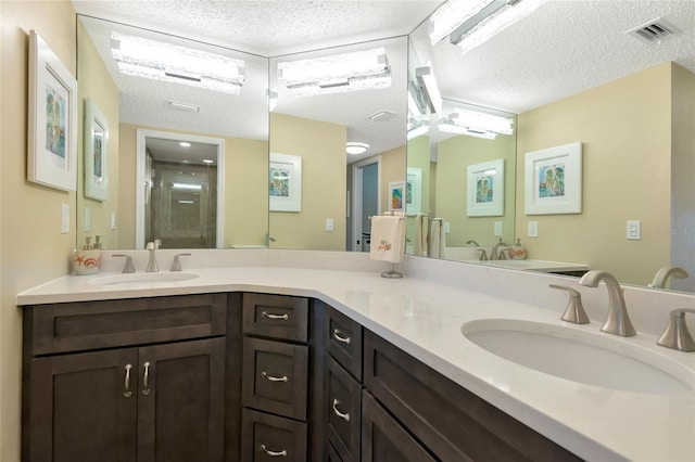 full bath with a textured ceiling, a stall shower, visible vents, and a sink