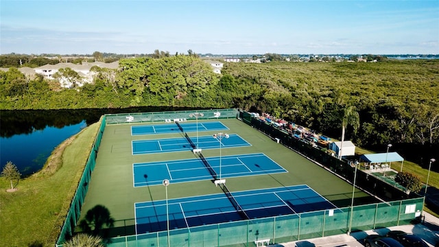 view of tennis court with a water view and fence