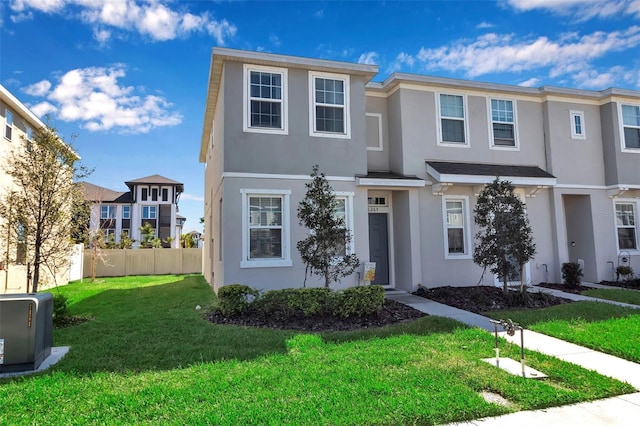 townhome / multi-family property with fence, a front lawn, and stucco siding