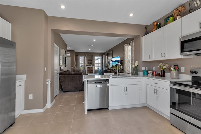 kitchen featuring stainless steel appliances, a peninsula, a sink, open floor plan, and light countertops