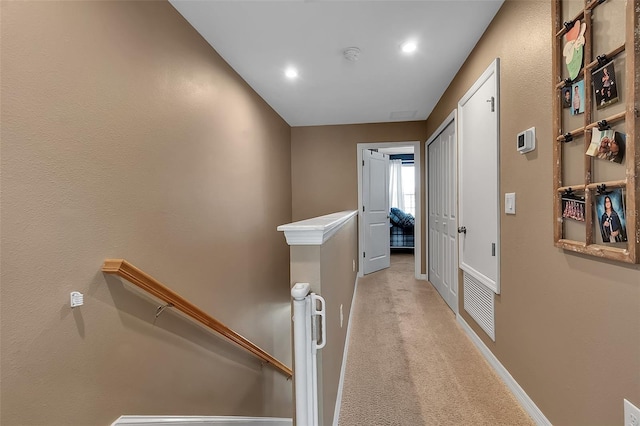 hallway with light carpet, visible vents, baseboards, and an upstairs landing