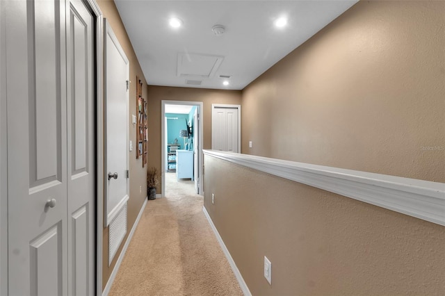 hallway featuring light carpet, attic access, visible vents, and baseboards