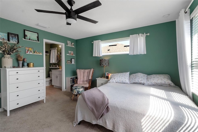 bedroom featuring ensuite bathroom, ceiling fan, visible vents, and light colored carpet