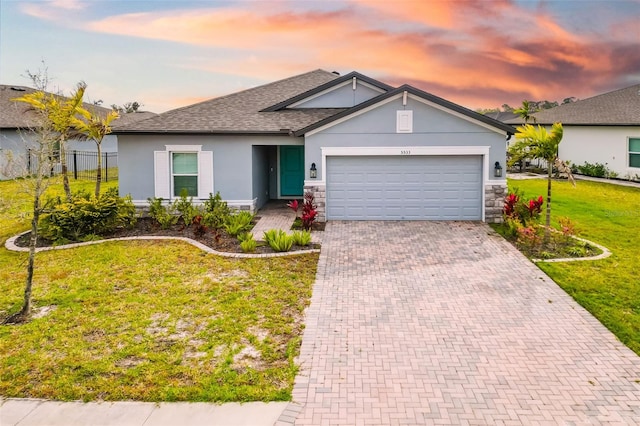 single story home featuring stucco siding, decorative driveway, a yard, stone siding, and an attached garage