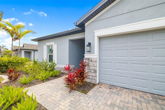 exterior space featuring stone siding, stucco siding, decorative driveway, and a garage