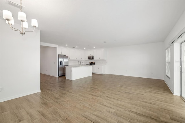 unfurnished living room featuring a sink, recessed lighting, light wood-style floors, and a chandelier