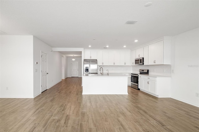 kitchen featuring light wood finished floors, backsplash, white cabinetry, stainless steel appliances, and light countertops