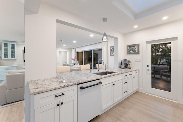 kitchen with light wood finished floors, open floor plan, a sink, light stone countertops, and dishwasher