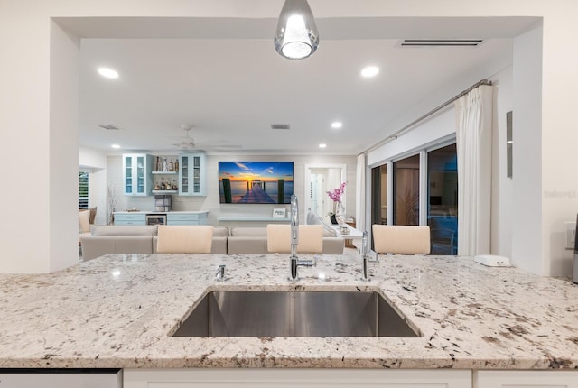 kitchen featuring open floor plan, light stone counters, a sink, and visible vents