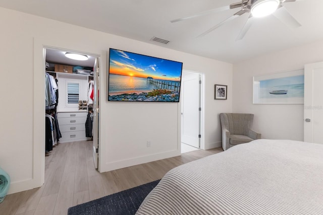 bedroom featuring light wood finished floors, visible vents, ceiling fan, a walk in closet, and a closet