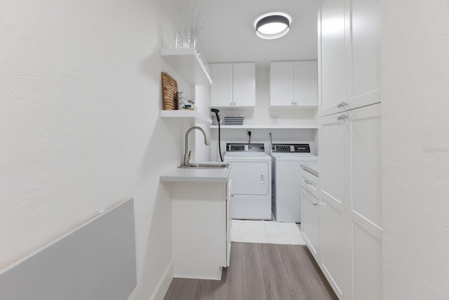 laundry area with wood finished floors, washing machine and clothes dryer, a sink, and cabinet space