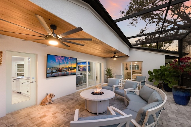 view of patio featuring glass enclosure, ceiling fan, and an outdoor living space with a fire pit