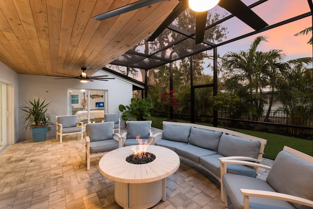 view of patio with a lanai, a ceiling fan, and an outdoor living space with a fire pit