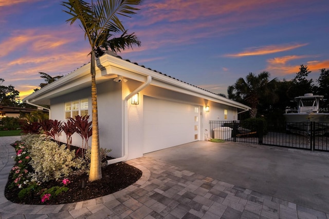 view of property exterior featuring a garage, a gate, fence, decorative driveway, and stucco siding