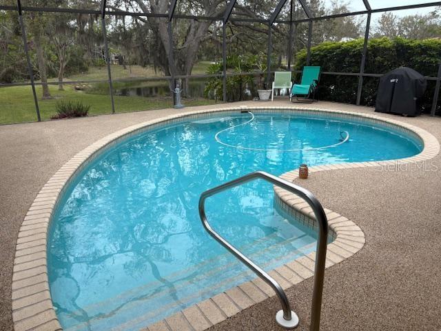 pool featuring glass enclosure, a patio, and grilling area