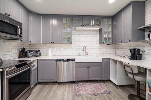 kitchen featuring light wood finished floors, gray cabinetry, stainless steel appliances, and a sink