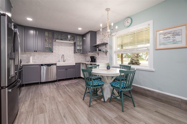 kitchen with gray cabinetry, a sink, tasteful backsplash, stainless steel appliances, and light countertops