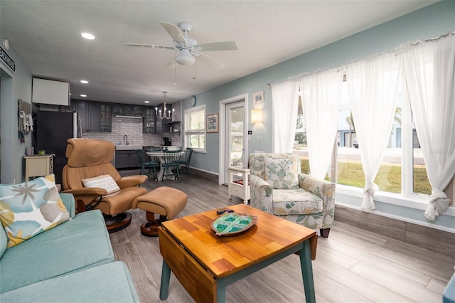 living room featuring baseboards, recessed lighting, ceiling fan with notable chandelier, and light wood-style floors