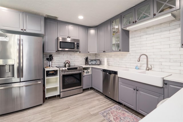 kitchen featuring gray cabinets, a sink, stainless steel appliances, light countertops, and decorative backsplash